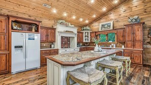 A kitchen with wooden cabinets, a central island with stools, and a refrigerator. - Timberstone: Luxury 4BR Cabin, Pool table, Arcade, Hot Tub, & Resort Pool (Sevierville)