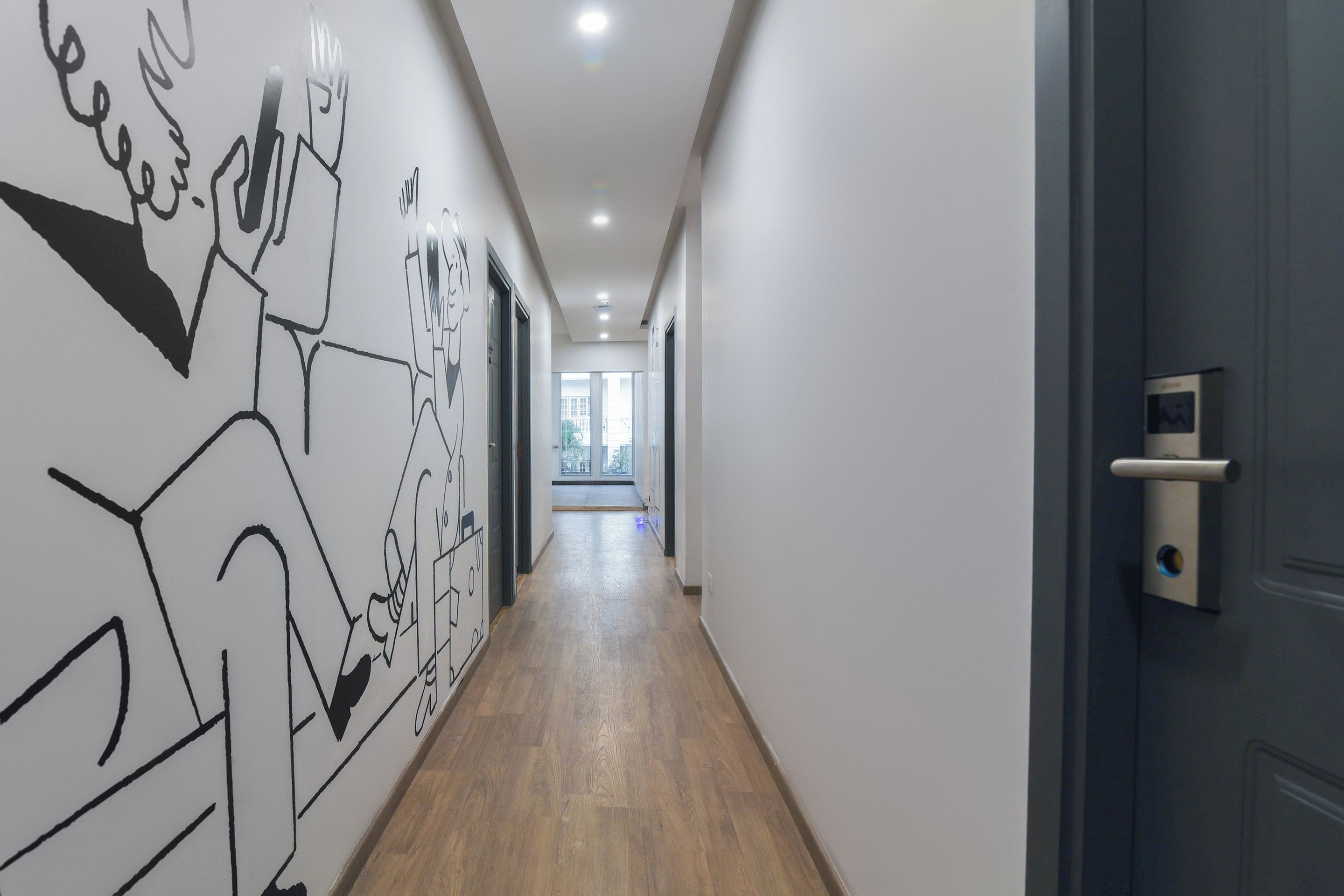 A hallway with a wooden floor, white walls, and a door with a security camera.
