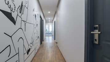 Un pasillo con piso de madera, paredes blancas y una puerta con cámara de seguridad.