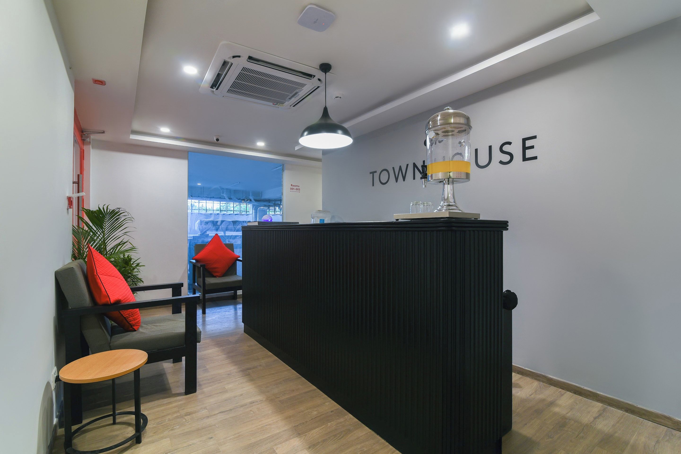Taulell de recepció amb un cartell que diu 'TOWNHOUSE USE' a l'interior modern amb un paviment de fusta, un taulell de recepció negre, una cadira amb coixinets vermells i una planta en test.