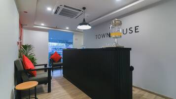 A reception desk with a sign reading 'TOWNHOUSE USE' in a modern interior with a wooden floor, a black reception desk, a chair with red cushions, and a potted plant.