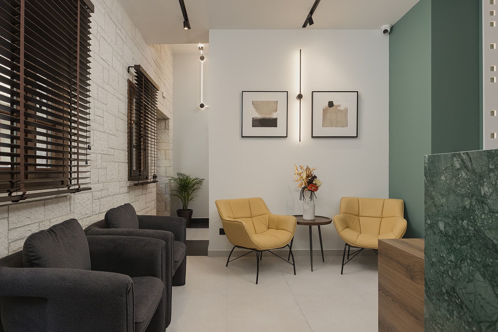 A modern waiting area with a stone wall, a potted plant, and two yellow chairs.