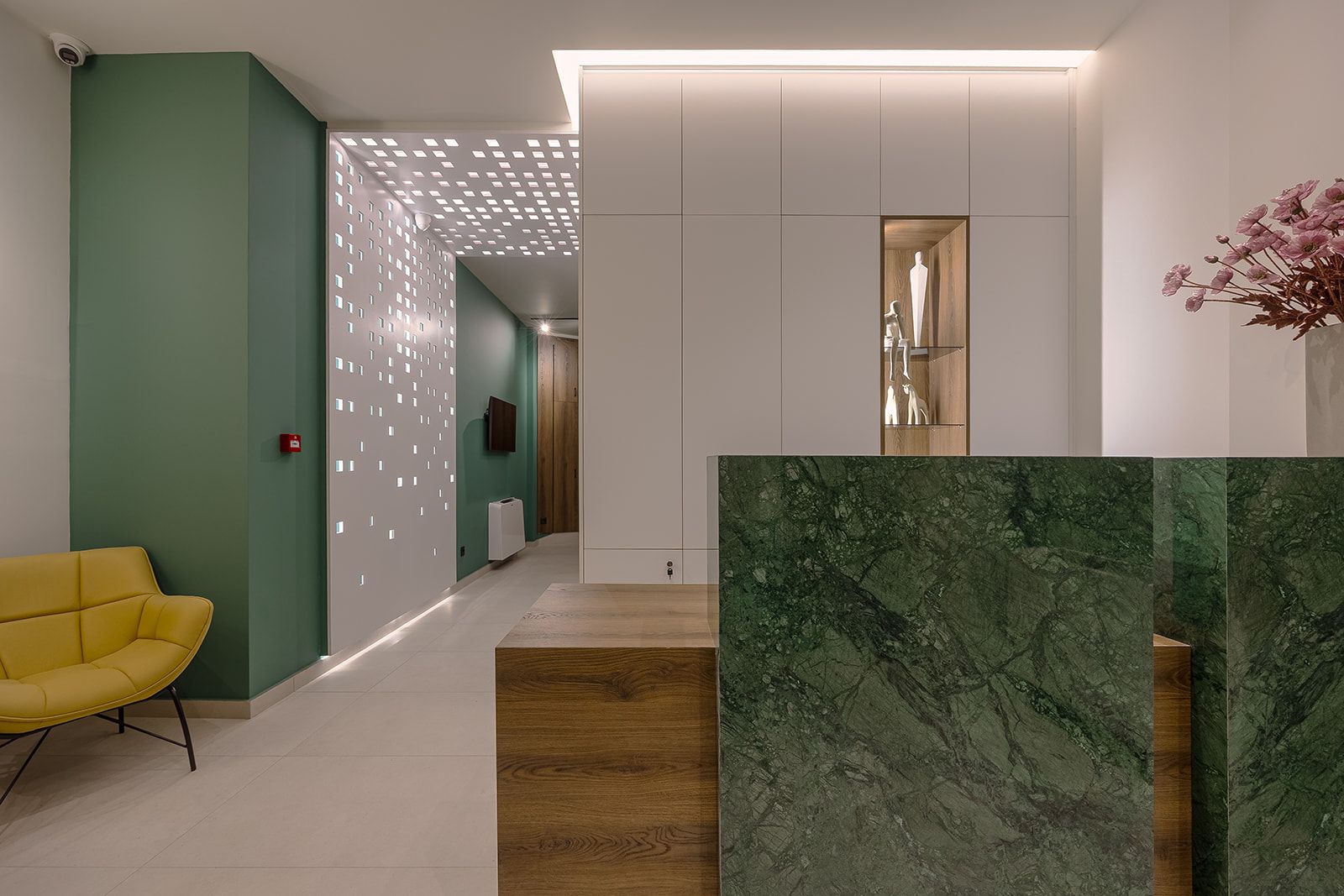Un interior moderno con una silla amarilla, piso de madera y una pared verde con diseño estampado.
