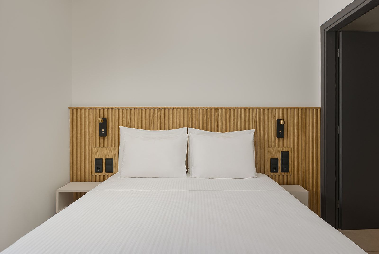 Habitación de hotel con cama, cabecero de madera, mesitas de noche y una puerta.
