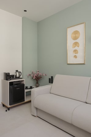 A modern living room with a sofa, a coffee machine, a small table with a vase of flowers, and a framed artwork on the wall. - Elysian Castle (Ioannina)