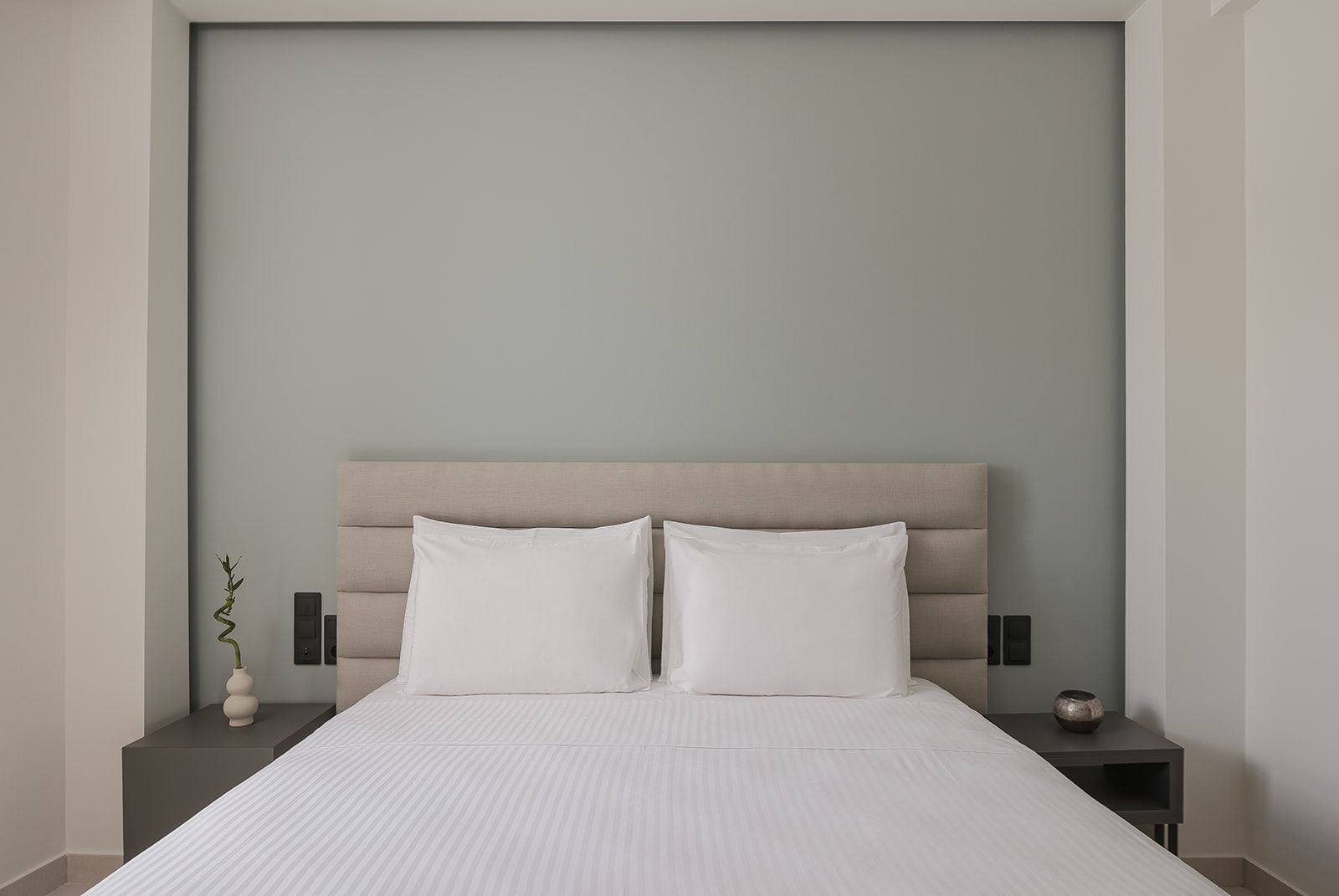 A bed with a headboard, two pillows, a bedside table with a vase, and a wall-mounted light fixture.