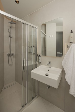 Un baño moderno con ducha envuelta en vidrio, un lavabo blanco y un espejo sobre él.