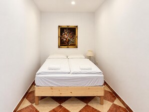 A single bed with a wooden frame and white bedding in a room with white walls and a patterned floor. - Your Vienna Chapter 1BR near Westbahnhof (Vienna)