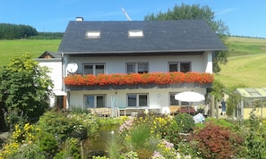 Ein zweistöckiges Haus mit einem Balkon, einem Teich und einem Garten.