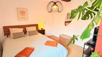A bedroom with a large bed, wooden beams, a hanging light fixture, a framed picture, and a potted plant.