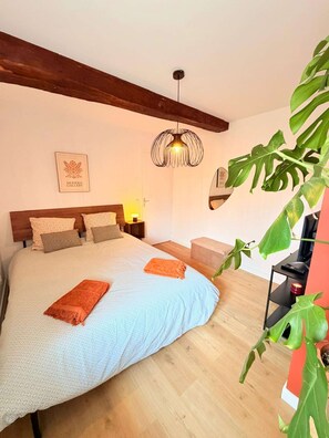 A bedroom with a large bed, wooden beams, a hanging light fixture, a framed picture, and a potted plant. - The Mid Century beaujolais (Lantignié)