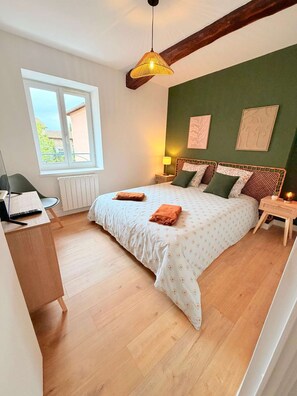A bedroom with a bed, a desk, a window, and a hanging light fixture.