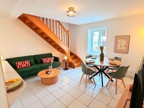 A modern living space with a green sofa, a wooden staircase, a dining area with a round table and chairs, and a large window providing natural light. - The Mid Century beaujolais (Lantignié)