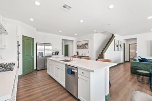 A modern kitchen with white cabinetry, a stainless steel refrigerator, and a built-in dishwasher. - The Trilogy: 27 Bedroom/18Bath/Sleeps 60/LazyRiver/Pickleball/GameRoom (Coachella)