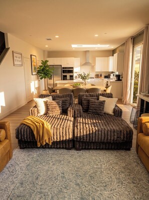 Ein modernes Wohnzimmer mit einem Ecksofa, einem Essbereich und einer Küche im Hintergrund.