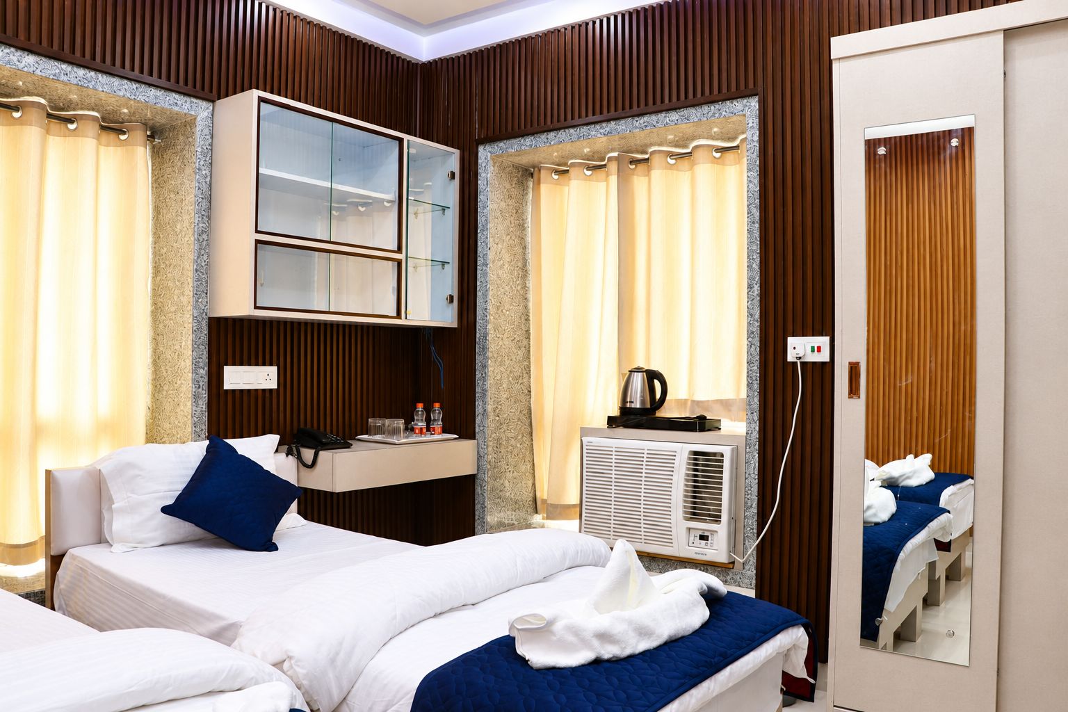 Ein Hotelzimmer mit zwei Betten, einer Minibar, einem Spiegel und einer Klimaanlage.