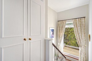 A white door with a brass handle, a staircase with a wooden handrail, and a window with floral curtains. - 2-Bed Chelsea Home with a private Terrace (London)