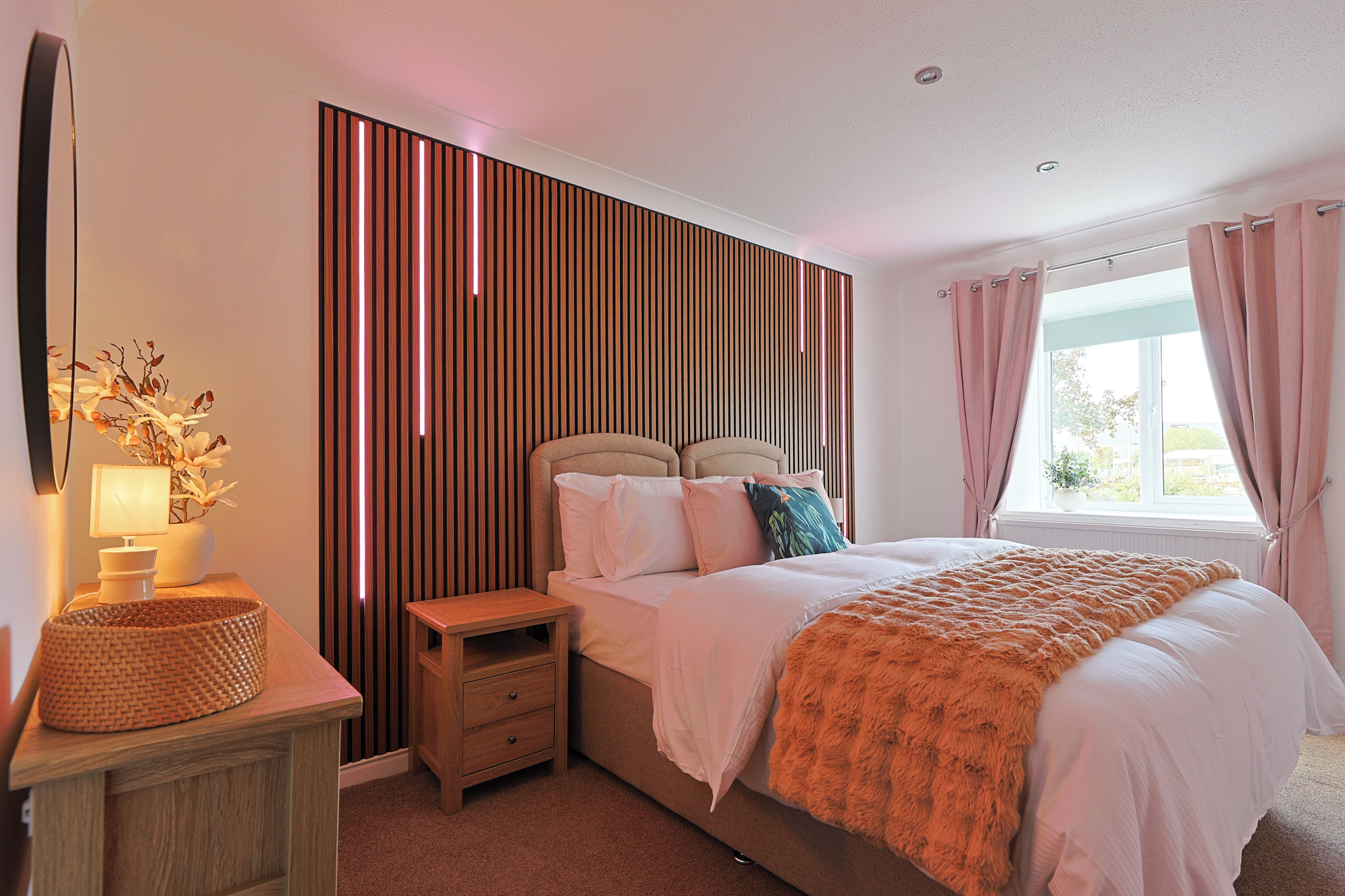 Ein Schlafzimmer mit einem Bett, einem Nachttisch, einer Lampe und einer Wand mit vertikalen Lamellen.