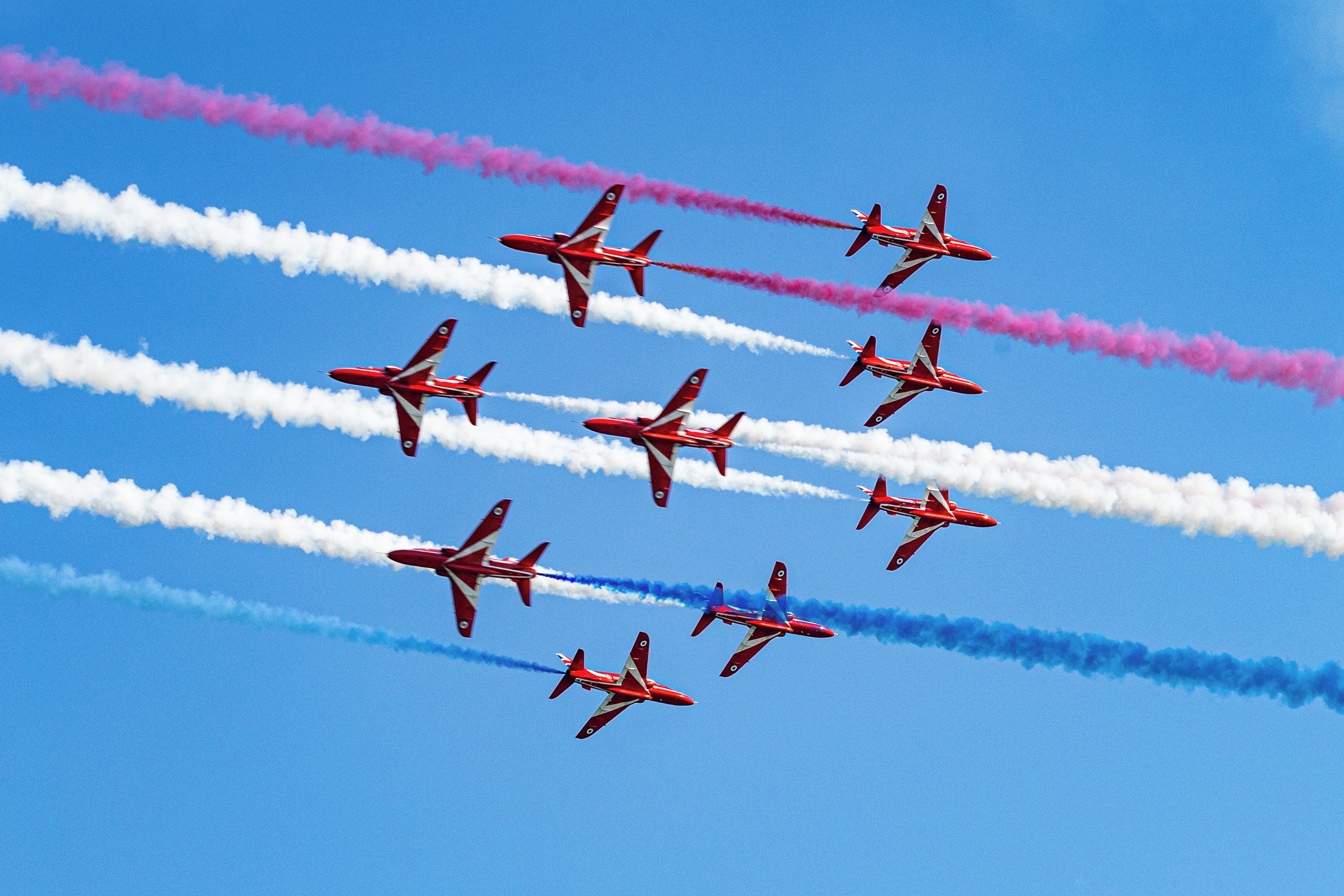 A group of red and white aircraft performing an aerial maneuver with smoke trails.