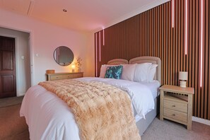 Une chambre à coucher comprenant un lit, des tables de chevet, un miroir et un mur avec des lambris en bois verticaux.