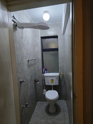 Ein kleines, schmales Badezimmer mit Toilette, einer Duschkabine und einer Deckenleuchte.