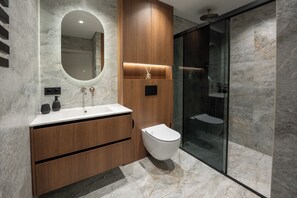 Un baño moderno con lavamanos de mármol, tocador de madera, cabina de ducha de vidrio y un inodoro.