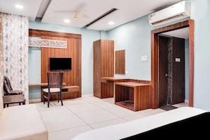 Habitación de hotel con cama, escritorio, silla, armario, televisor y aire acondicionado.