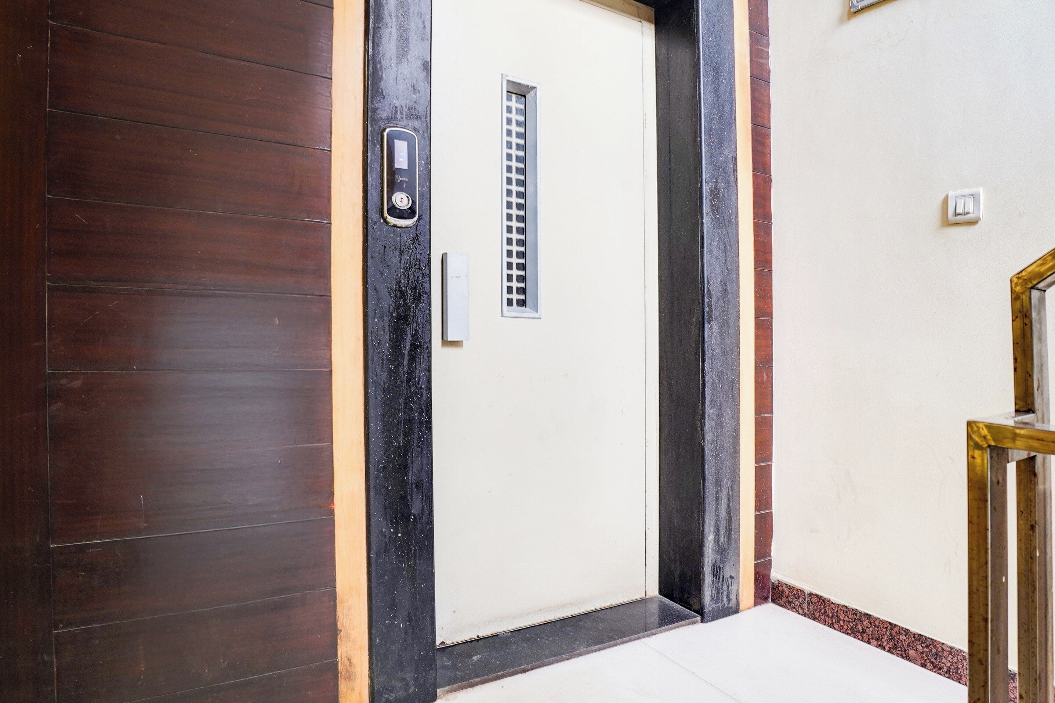 A door with a metal handle and a small window, flanked by dark wooden panels and a contrasting black frame.