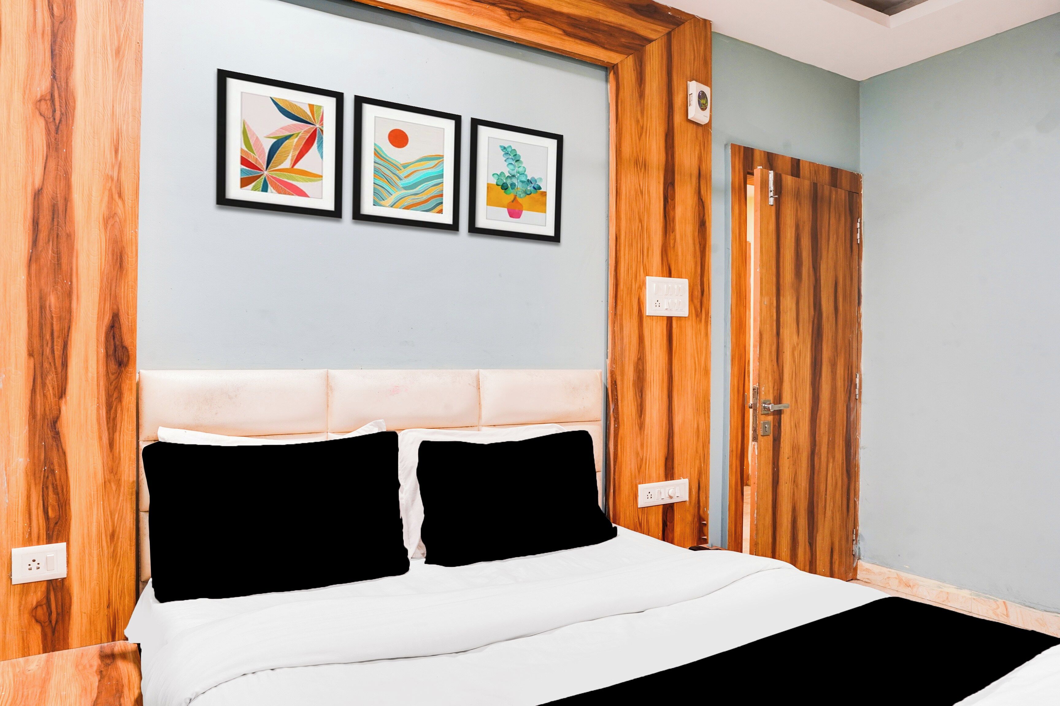 A bedroom with a bed, a wooden headboard, and three framed artworks on the wall.