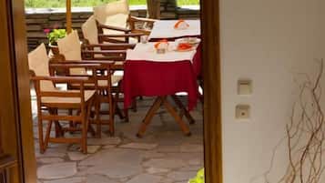 Una escalera de madera que lleva a un área de comedor al aire libre con mantel rojo, sillas y una planta en maceta.