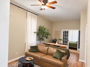 A living room with a brown leather sofa, a small round table, a ceiling fan, and a potted plant. - Chic Chicago Retreat, Stylish & Cozy Escape: 3 bedroom (Chicago)
