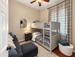 A bedroom with a bunk bed, a bedside table with a lamp, a mirror, a sofa, and a patterned curtain. - Chic Chicago Retreat, Stylish & Cozy Escape: 3 bedroom (Chicago)