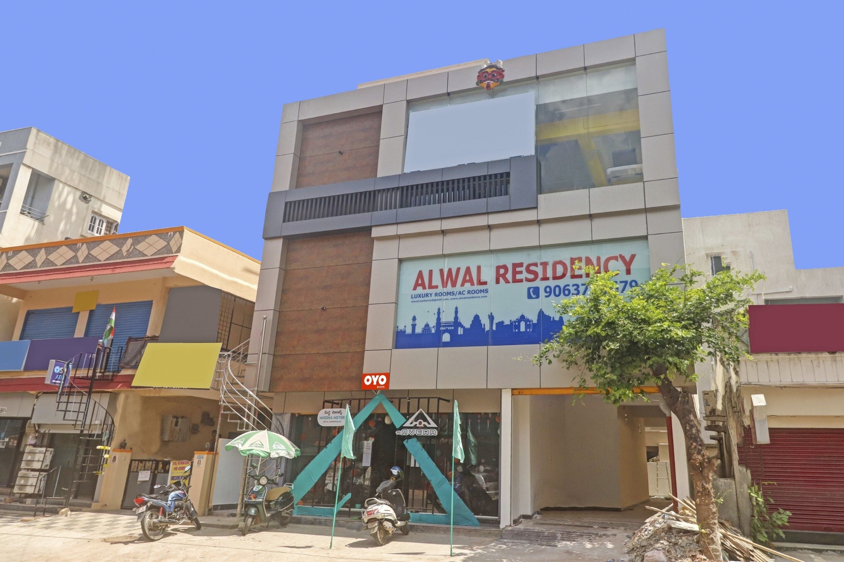 A building with a sign for Alwal Residency offering luxury rooms and AC rooms.