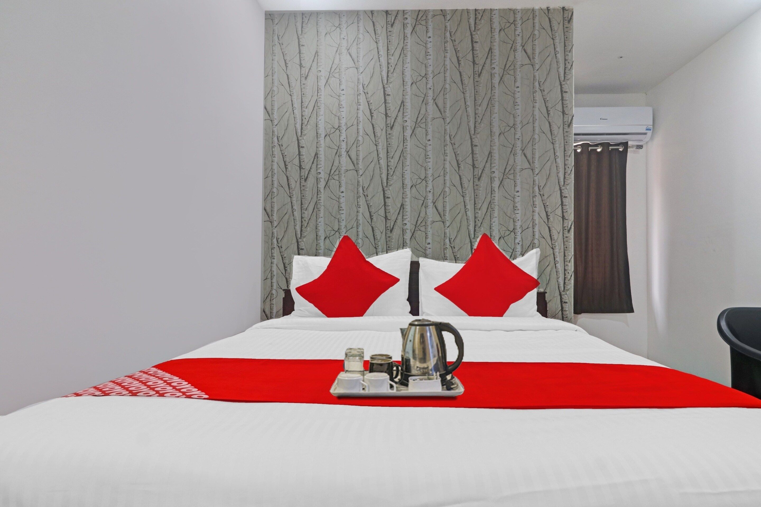 Una habitación de hotel con cama, un plaid rojo, un hervidor y una cafetera sobre la cama.