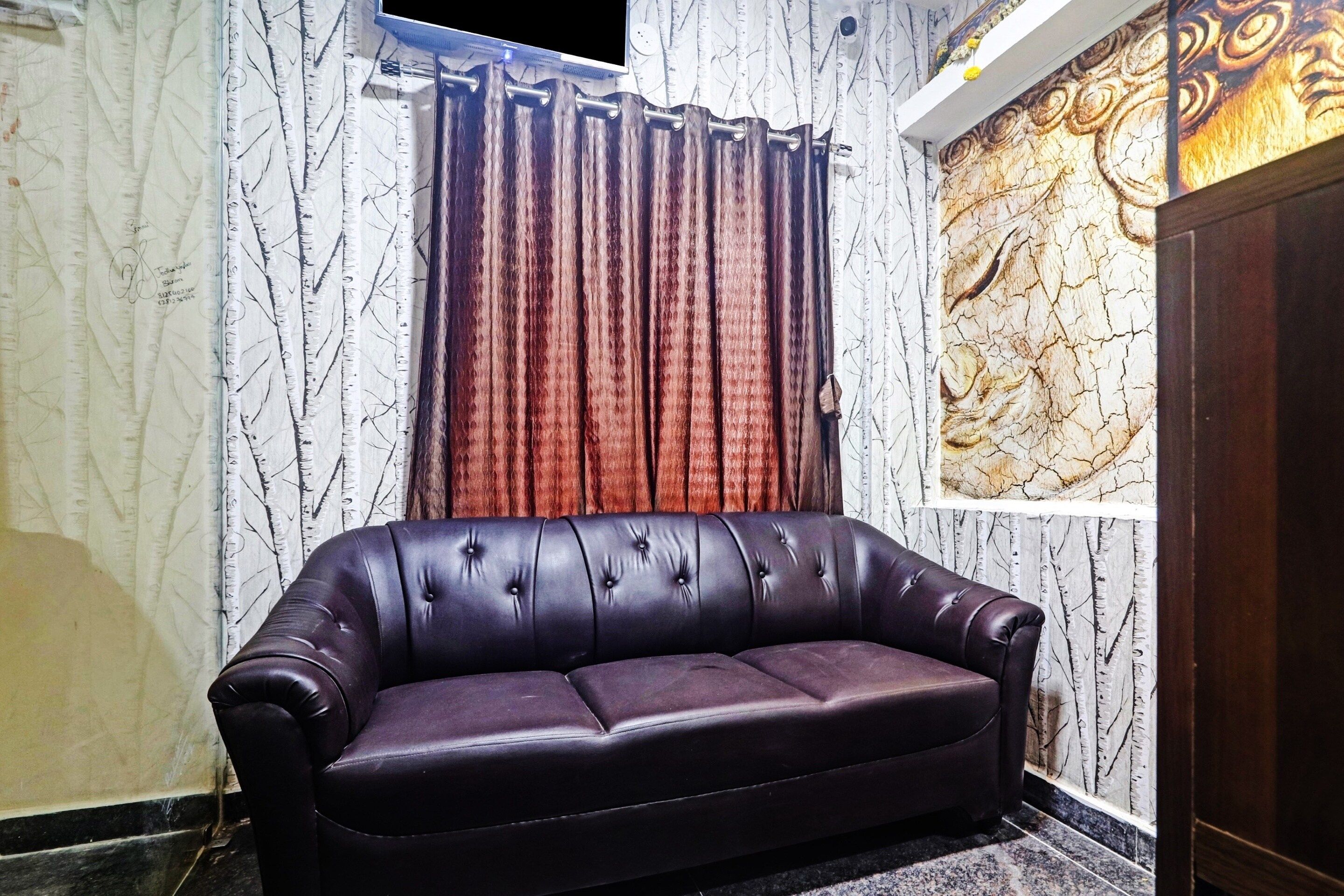 Un sofá de cuero oscuro en una habitación con pared de diseño marmolado y una pieza decorativa grande sobre la ventana.
