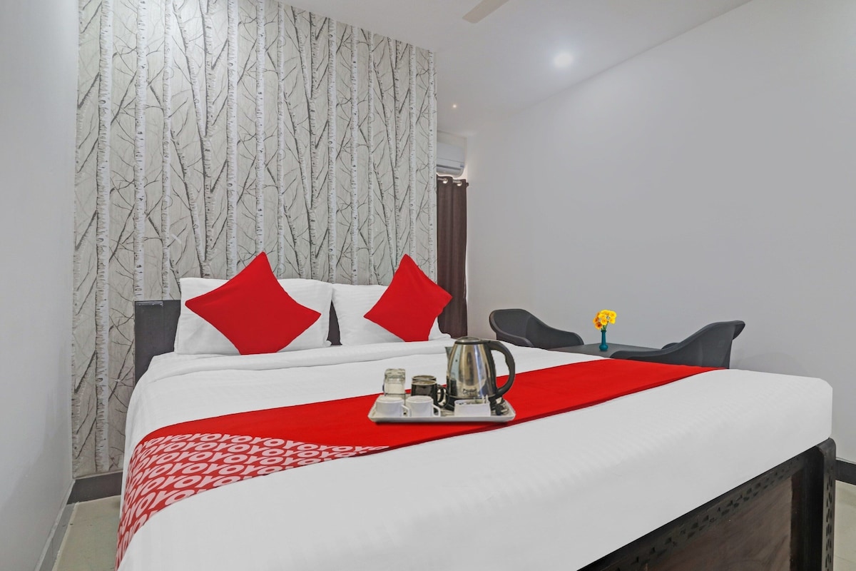 A hotel room with a bed, pillows, a coffee maker, and a vase with flowers.