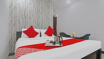 Una habitación de hotel con cama, almohadas, cafetera y un florero con flores.