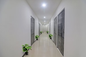 A corridor with doors on both sides, potted plants, and a tiled floor.