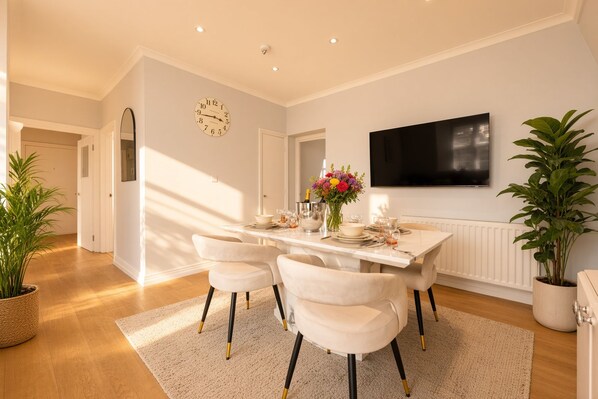 A dining area with a marble table, white chairs, a clock, a flat-screen TV, and potted plants. - Piccadilly Circus Skyline Apartment - 2Bed 2Bath (London)