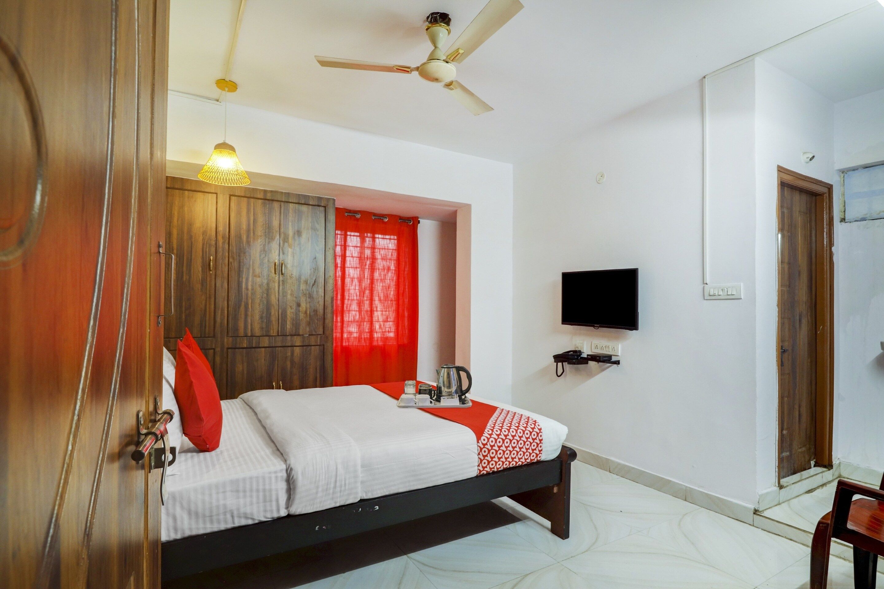 Quarto de hotel com cama, televisão, ventoinha no teto e guarda-roupa de madeira.