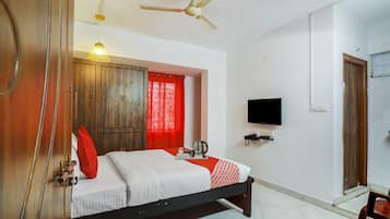 Quarto de hotel com cama, televisão, ventoinha no teto e guarda-roupa de madeira.