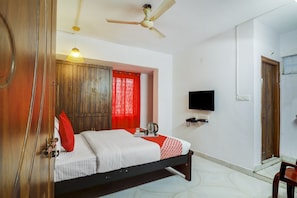 Quarto de hotel com cama, televisão, ventoinha no teto e guarda-roupa de madeira.
