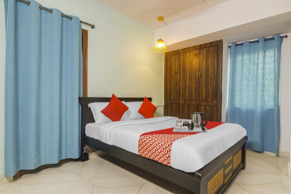 Cama com roupa de cama branca e almofadas vermelhas, guarda-roupa de madeira e bandeja com chaleira e chávenas.
