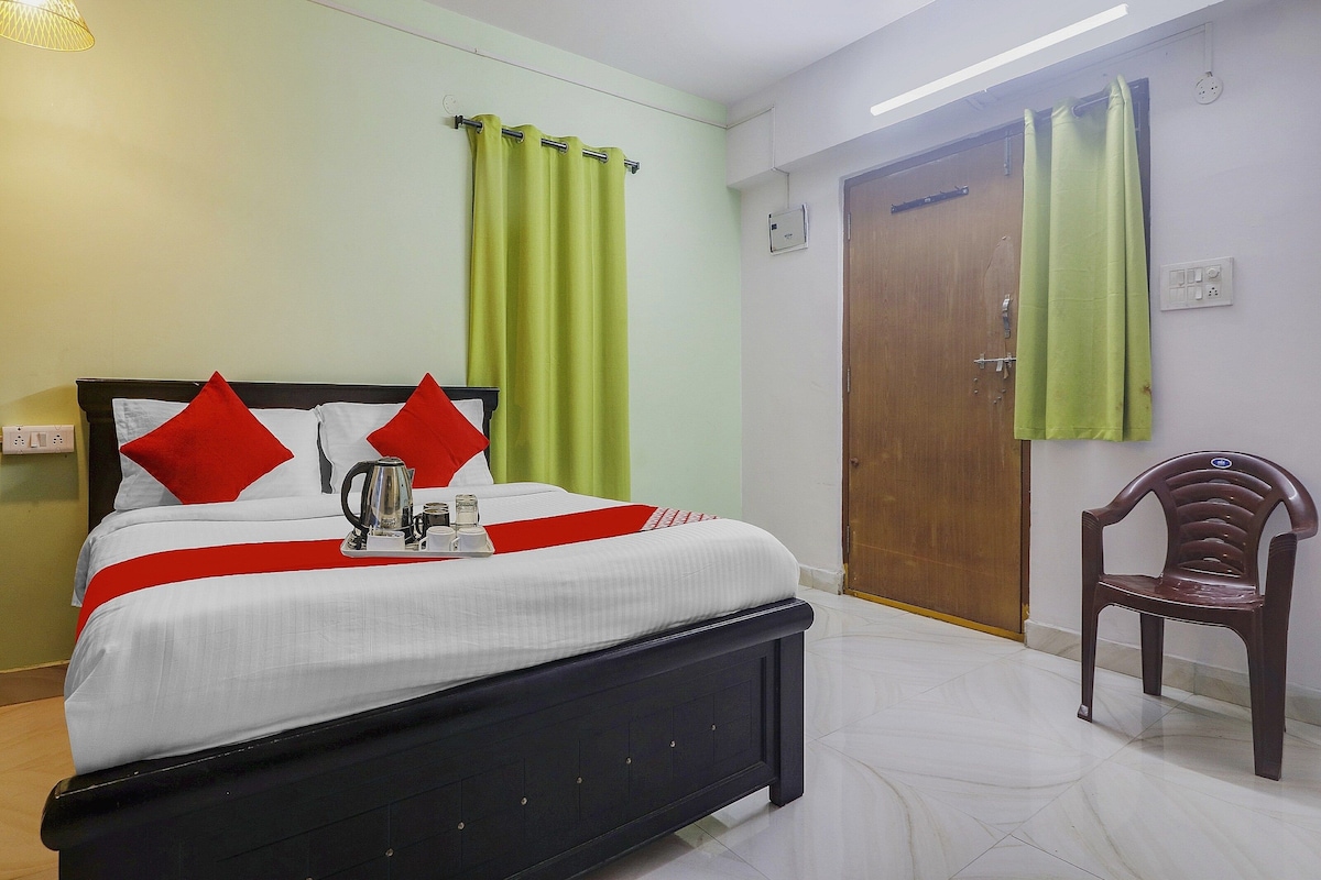 Una habitación de hotel con cama, una silla, una puerta y un ventanal con cortinas.