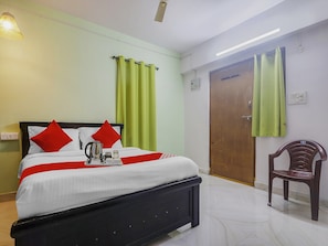 Una habitación de hotel con cama, una silla, una puerta y un ventanal con cortinas.