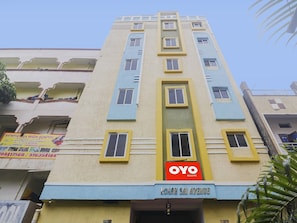 Um edifício de vários andares com fachada em amarelo e azul destacada, um letreiro indicando OYO Rooms e um letreiro para a Richards High School.