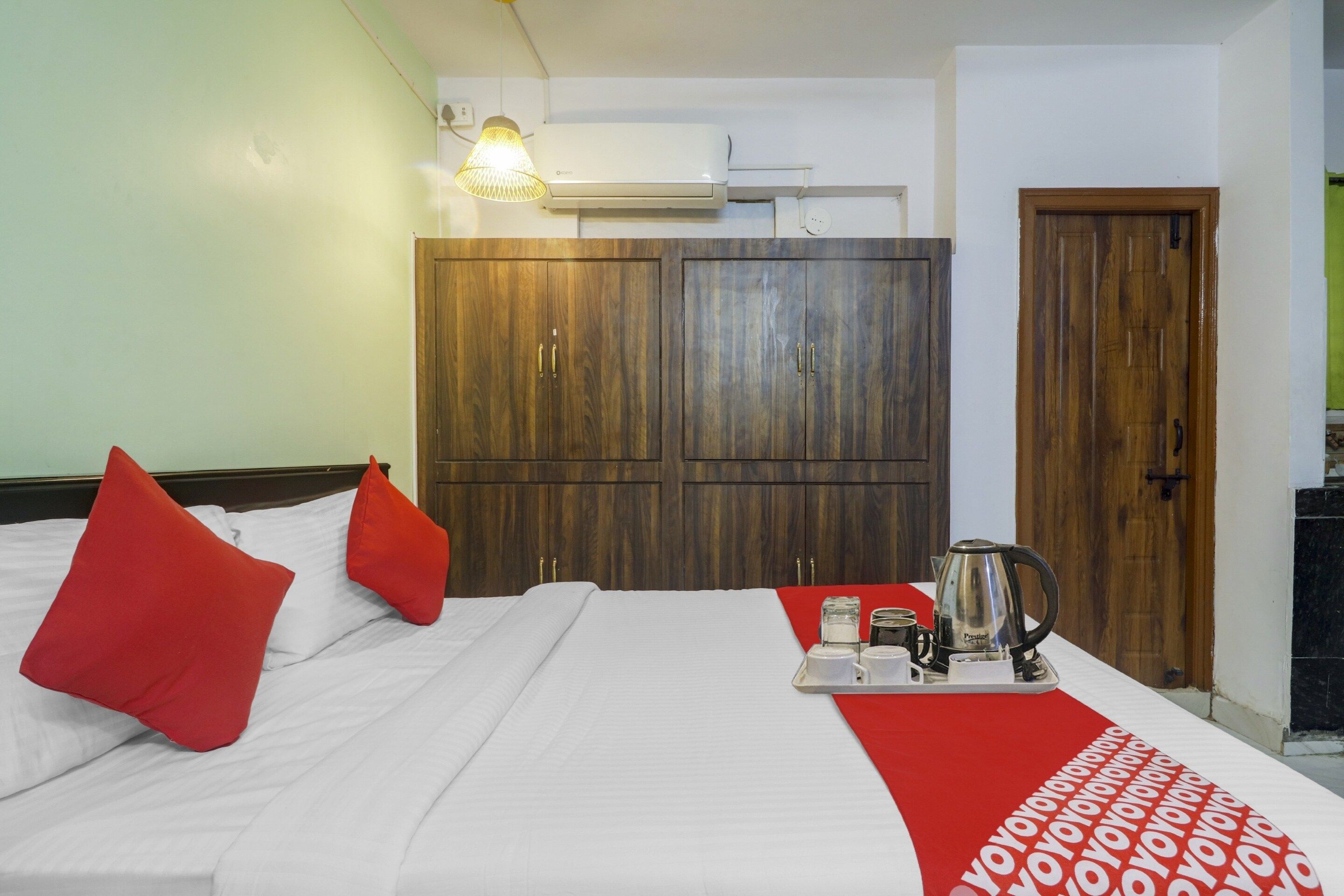 A hotel room with a bed, red pillows, a tray with a coffee pot, and a red and white patterned runner.