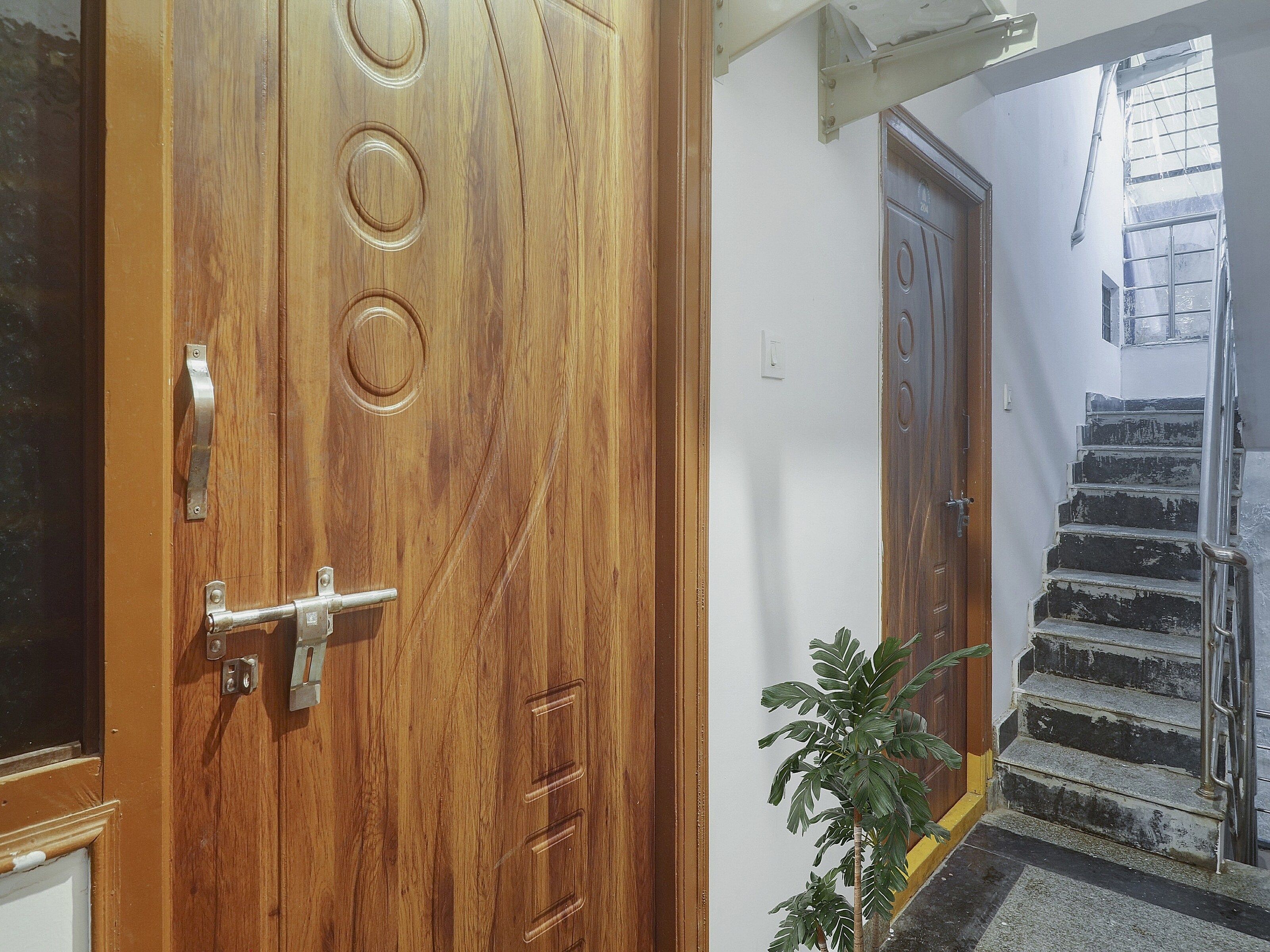 Una puerta de madera con picaporte y cerradura, una escalera con barandillas de metal y una planta en maceta.