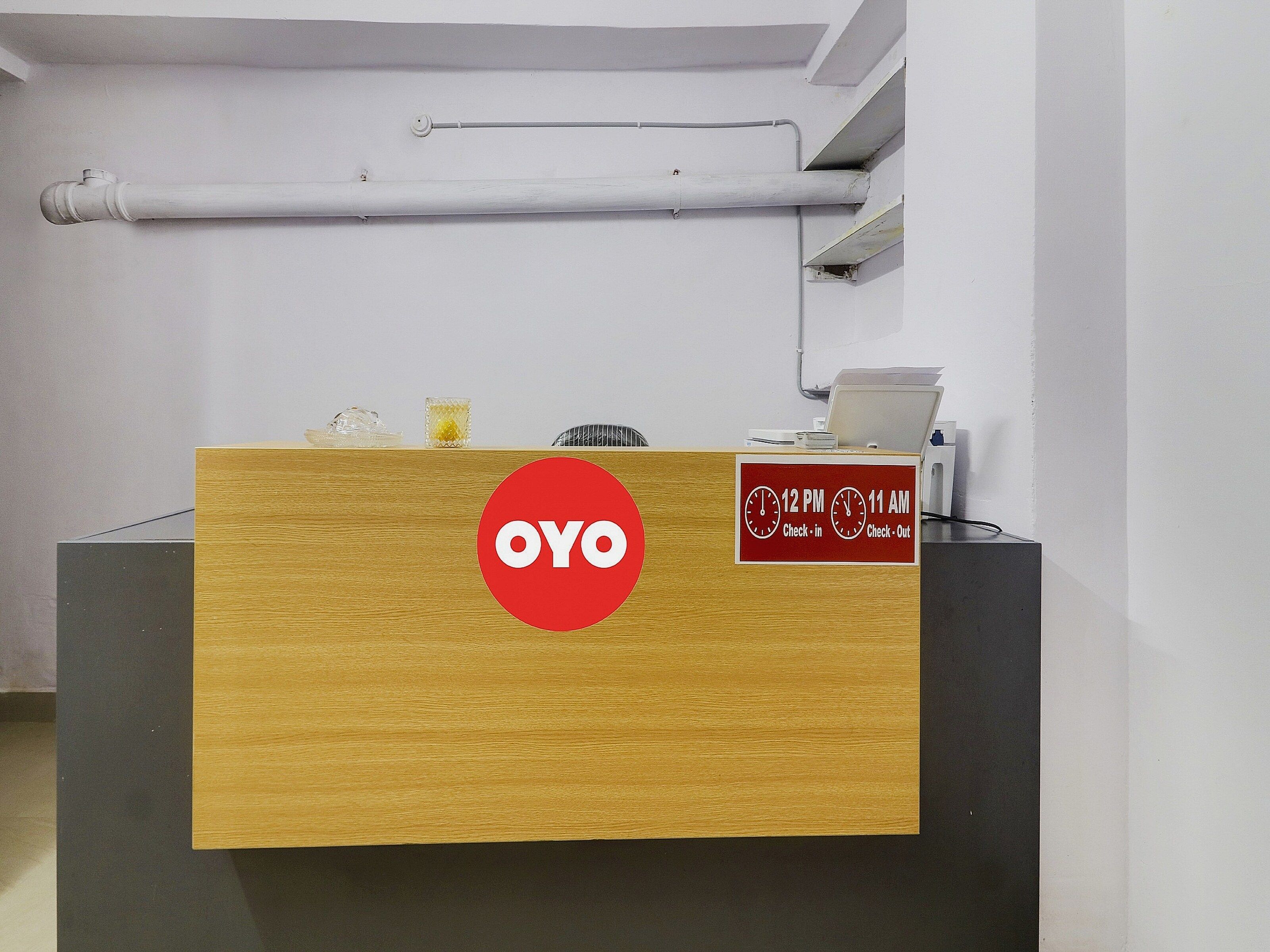 A reception desk with a wooden top, a red logo, and a sign indicating check-in and check-out times.
