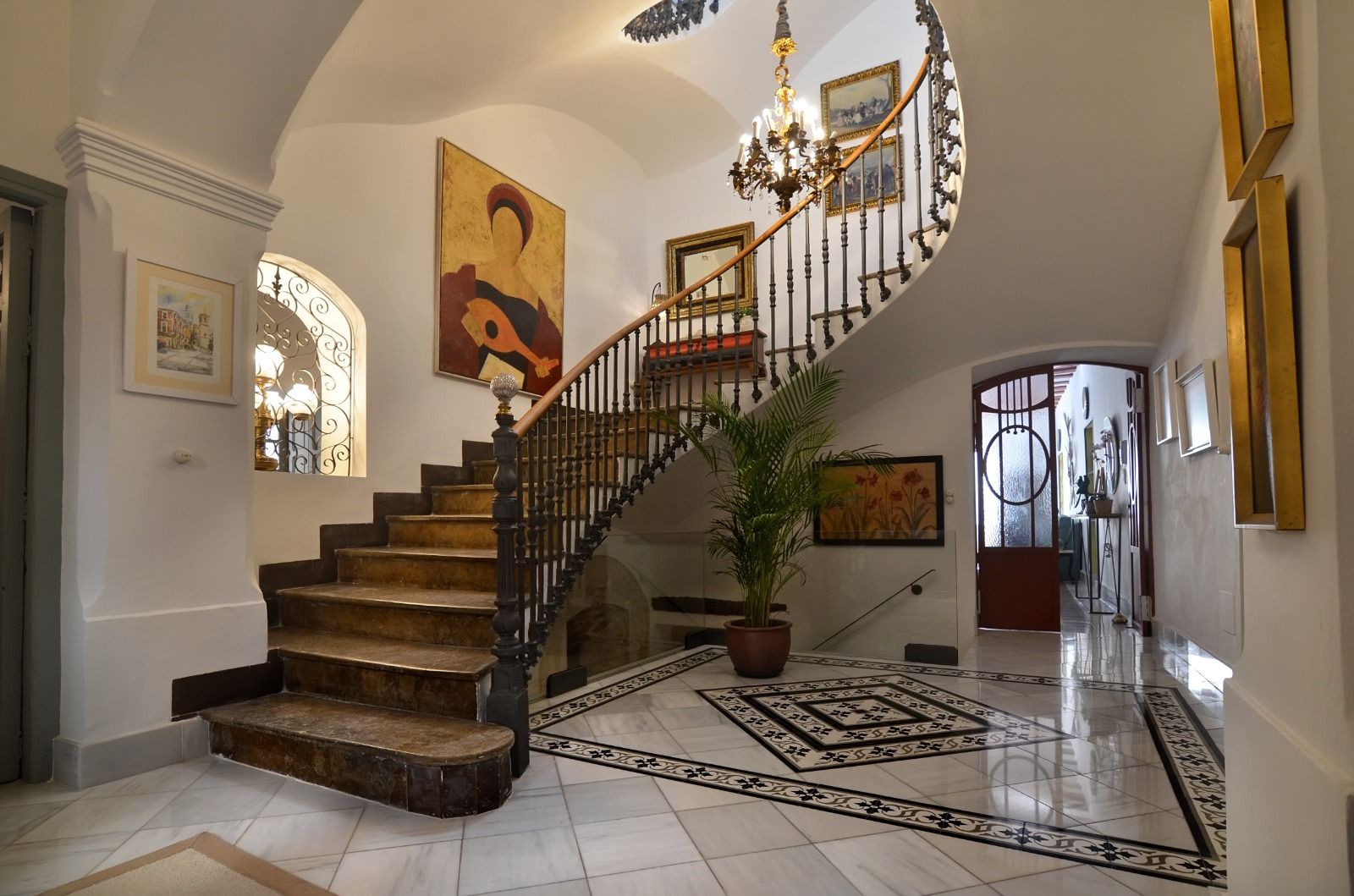 Una imponente escalera con un candelabro, un cuadro grande y una planta en maceta.